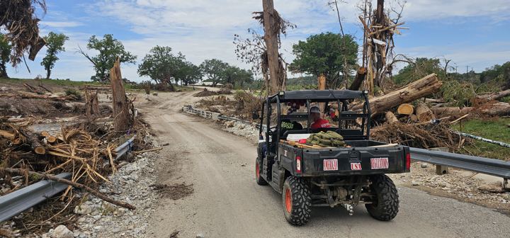 A utility vehicle hauls debris along a flood-damaged road