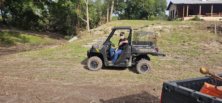 A volunteer drives a utility vehicle across a cleared lot