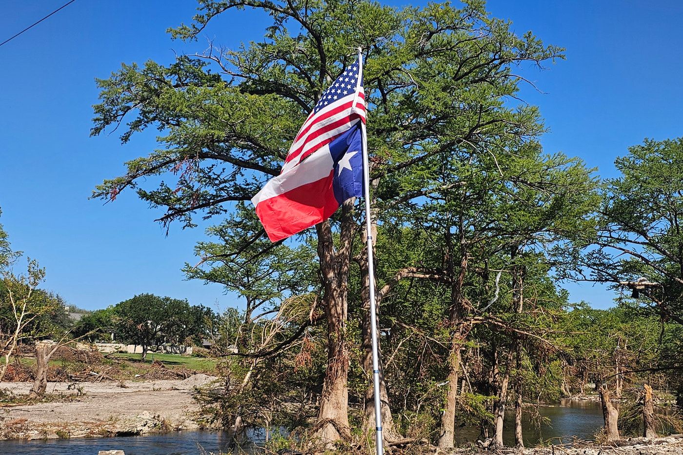Texas and American flags fly beside a flooded riverbank